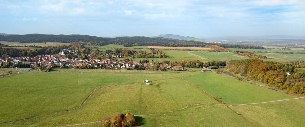 An aerial view of a rural area with a small village, green fields, and distant hills.