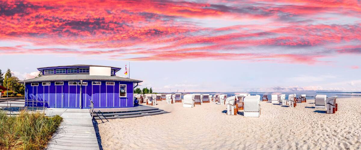 A beach with a purple building, white beach chairs, and a wooden boardwalk.