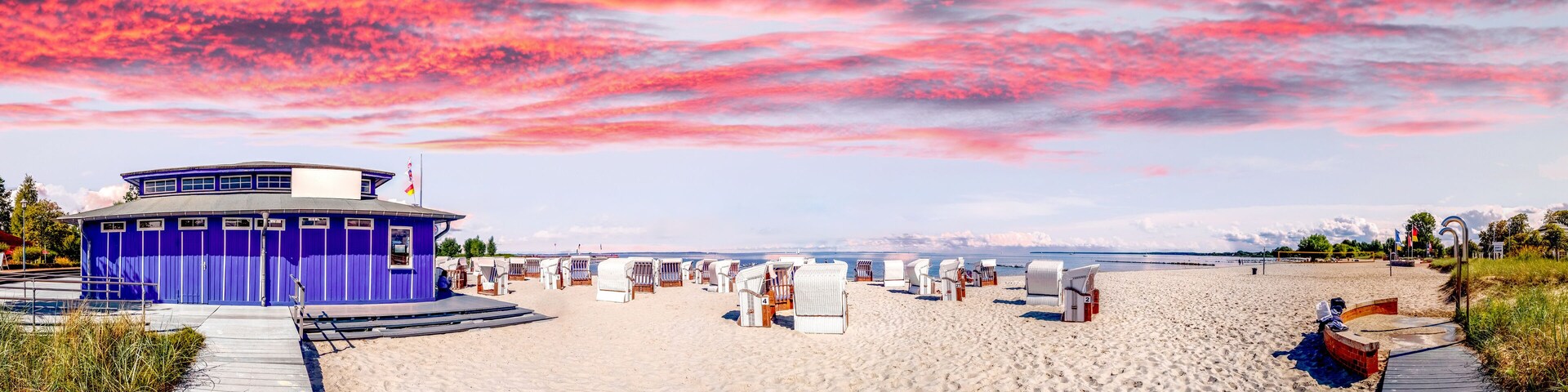 A beach with a purple building, white beach chairs, and a wooden boardwalk.