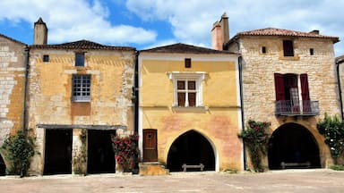 Une rangée de bâtiments historiques aux façades en pierre, aux portes en arc de cercle et aux volets rouges.