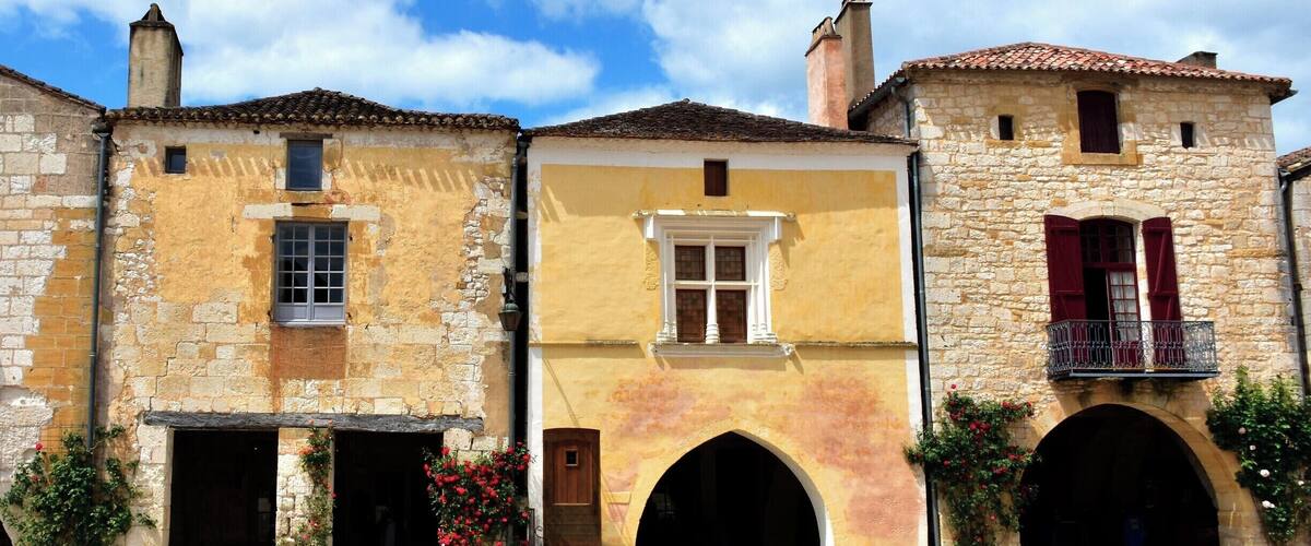 A row of historic buildings with stone facades, arched doorways, and red shutters.