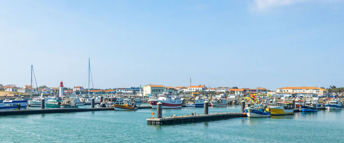 A marina with various boats docked, a lighthouse, and buildings with orange roofs.