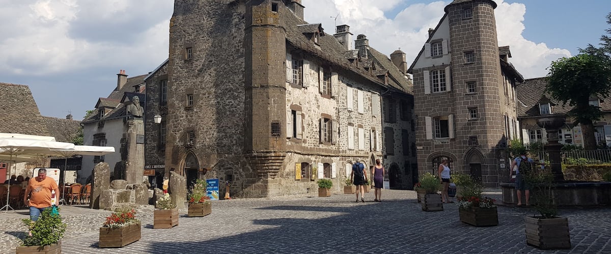 A historic stone building with a tower, cobblestone street, and potted plants.