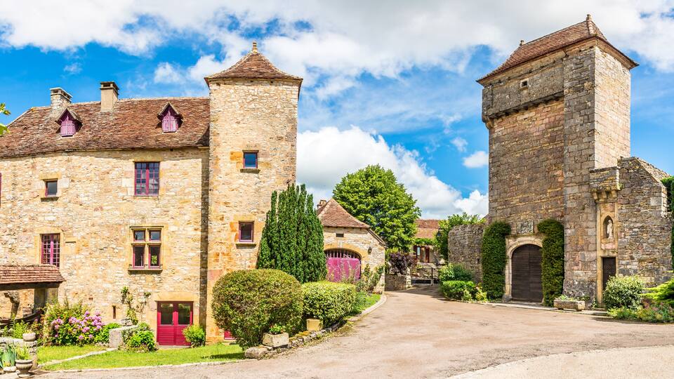 A stone building with a tower, surrounded by greenery and a clear sky.