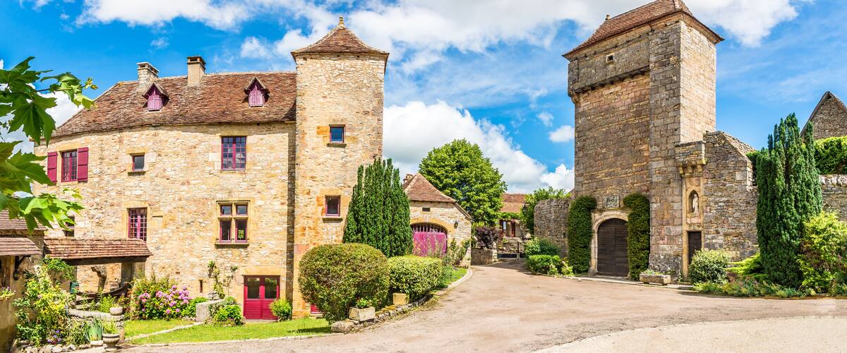 A stone building with a tower, surrounded by greenery and a clear sky.