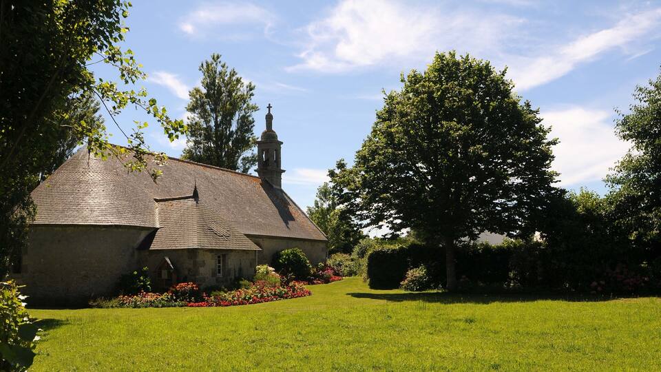 A stone church with a bell tower, surrounded by a well-maintained lawn and flowering shrubs.