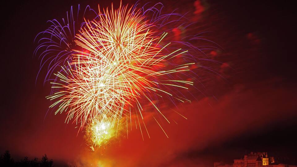 A night sky with a large firework display over a cityscape.