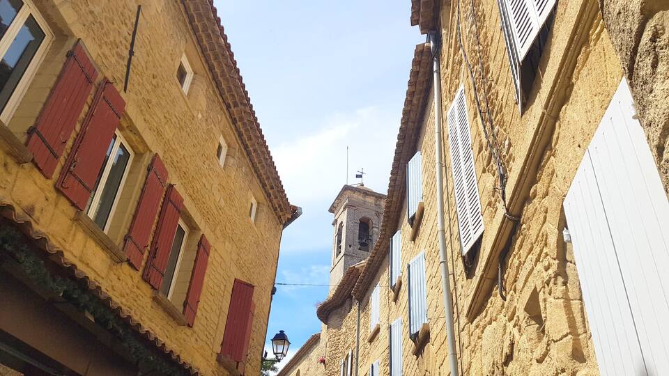 A narrow street with old buildings, red shutters, and a bell tower.