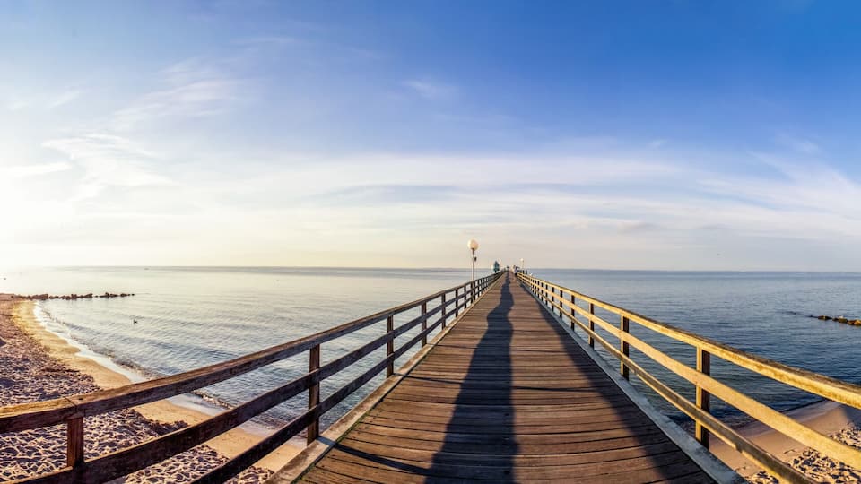 A beach with a wooden pier extending into the sea, a sandy shore, and a clear sky.