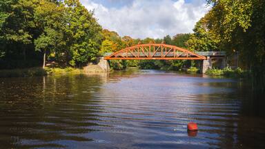 Autumn colors surrounds the red bridge Pyttebron over Ronne river which is built 1904 and still in use today in Angelholm, Sweden.