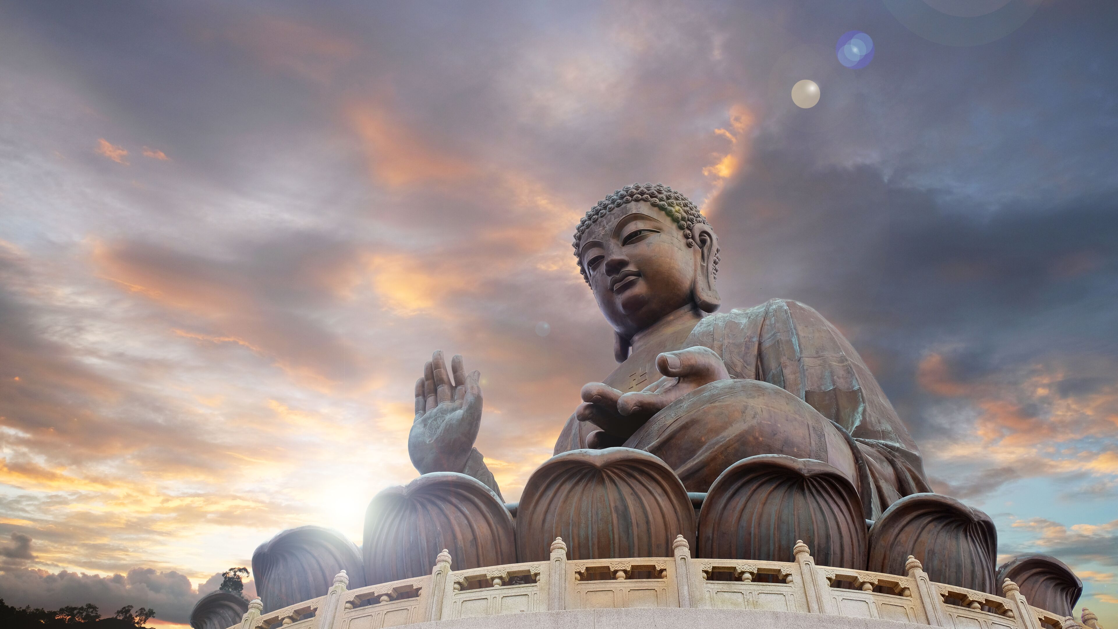 A large Buddha statue with a serene expression, surrounded by a circular railing, set against a dramatic sky with clouds.