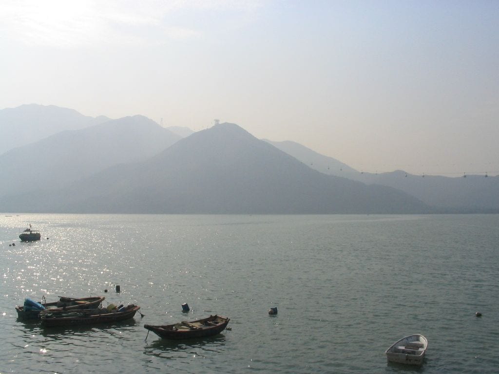 Un lago tranquilo con varias embarcaciones, una cadena montañosa distante y un cielo despejado.