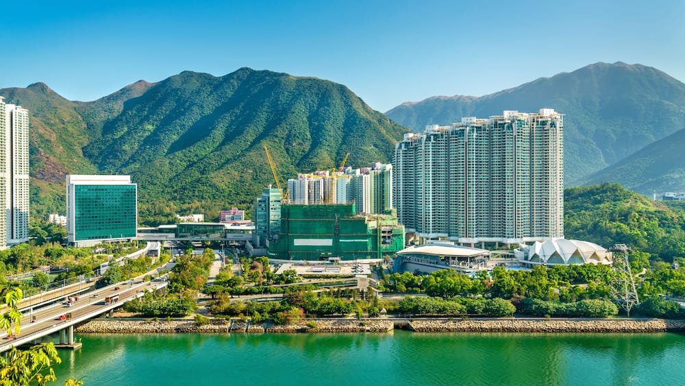 A cityscape with modern high-rise buildings, a bridge, and a mountain range in the background.