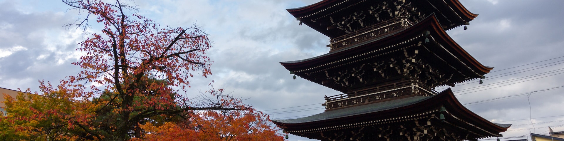 Una pagoda japonesa tradicional de varios niveles, rodeada de follaje otoñal y un farol de piedra.