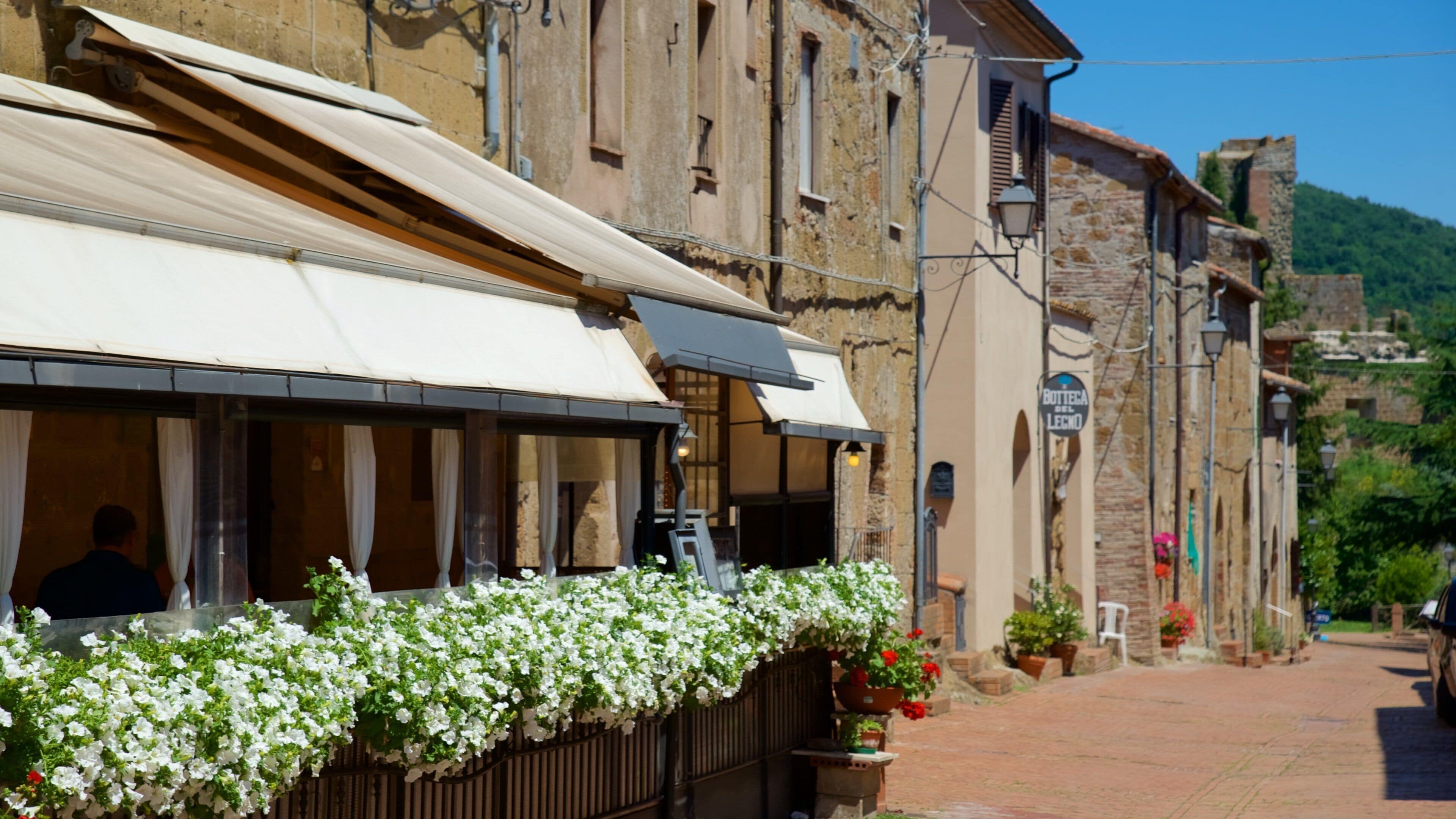 A street with a restaurant, white flowers, and a sign reading "Bottega del Lecco".