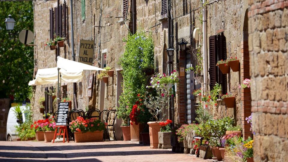 A narrow street lined with old buildings, potted flowers, and a sign for a pizza restaurant.