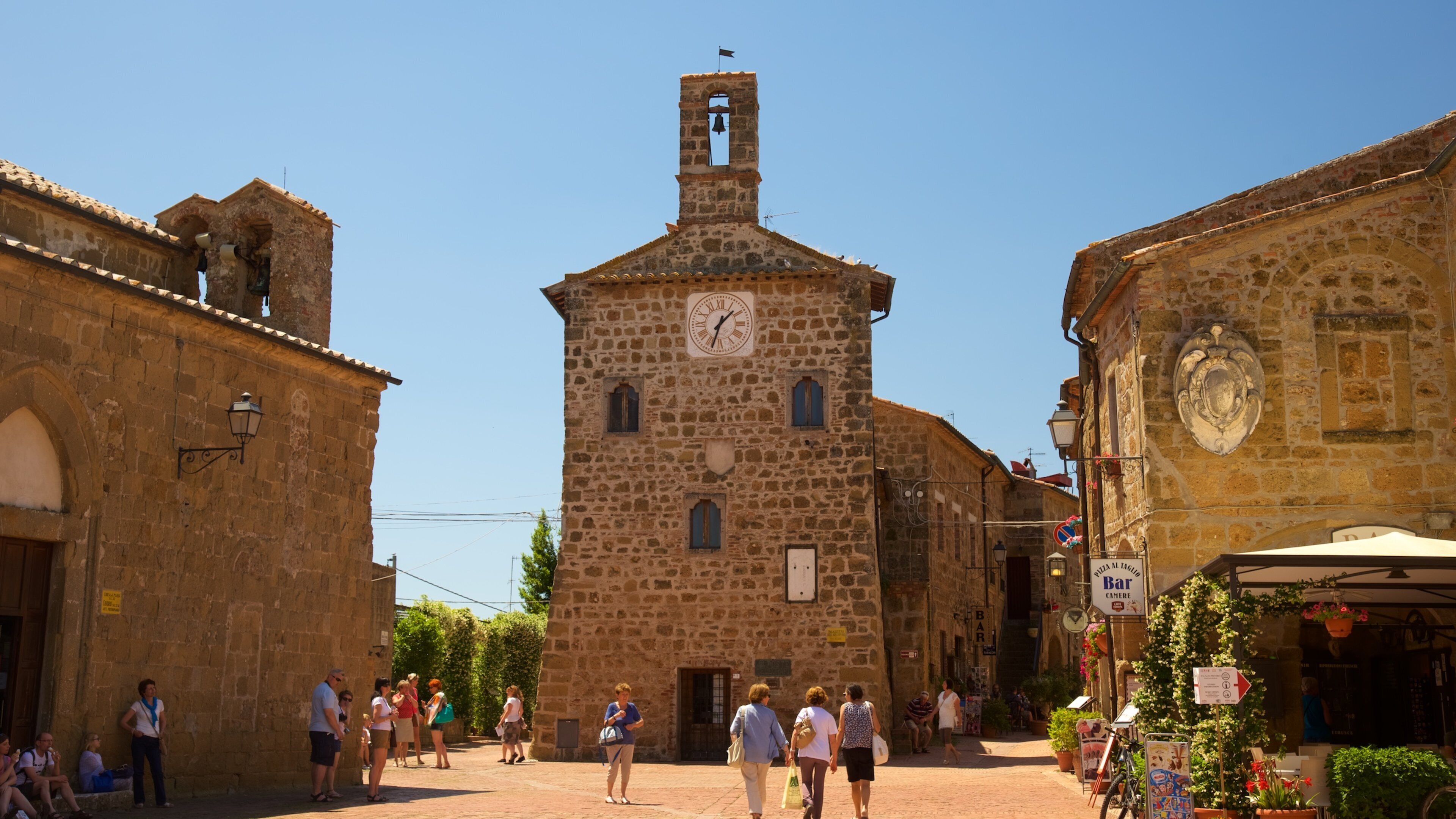 A historic stone building with a clock tower, cobblestone streets, and people walking.