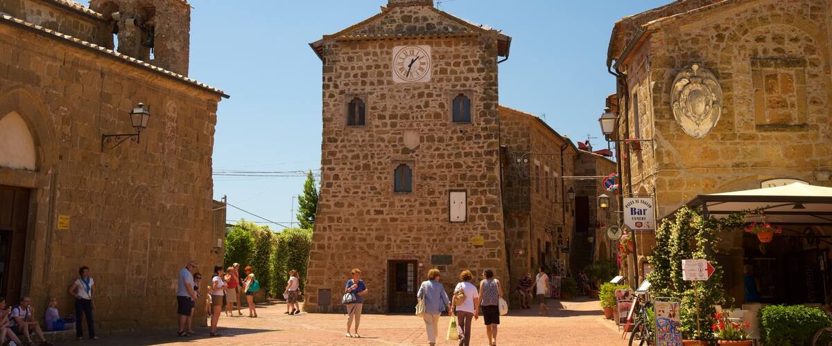 A historic stone building with a clock tower, cobblestone streets, and people walking.