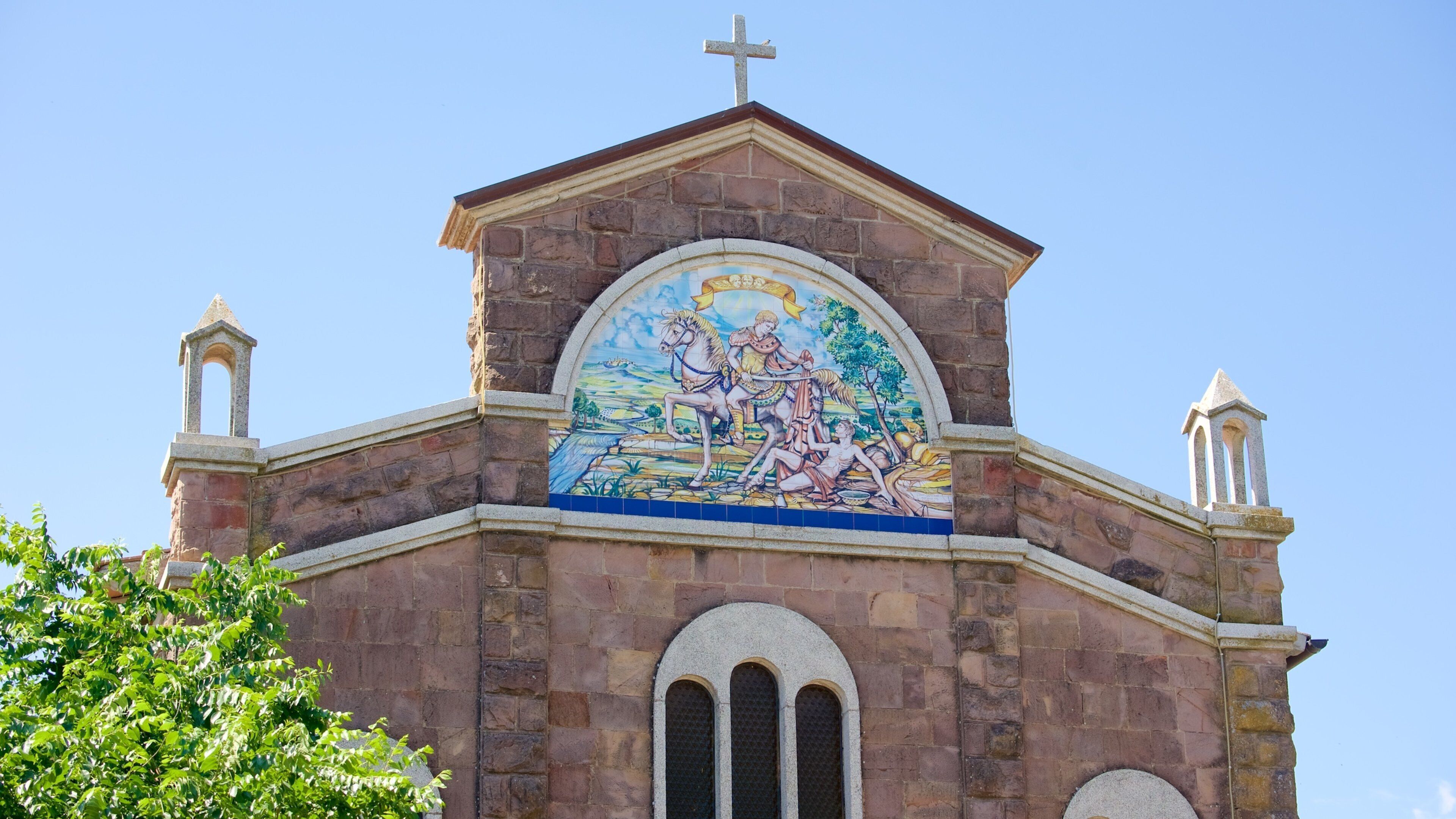 Una iglesia con un mural de un jinete y un caballo, una cruz en la parte superior y dos campanarios.