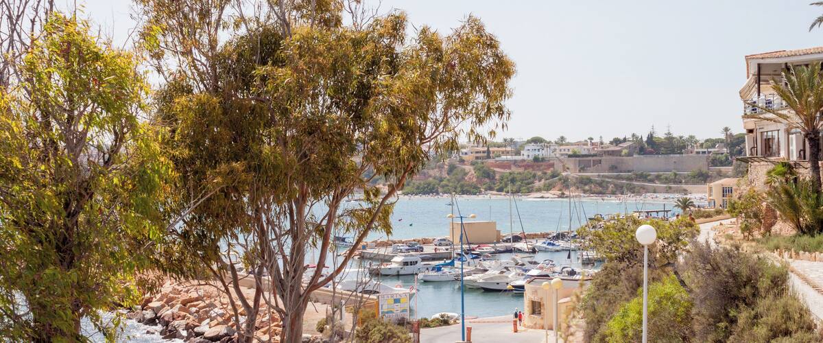 A coastal town with a marina, rocky shoreline, and buildings along the sea.