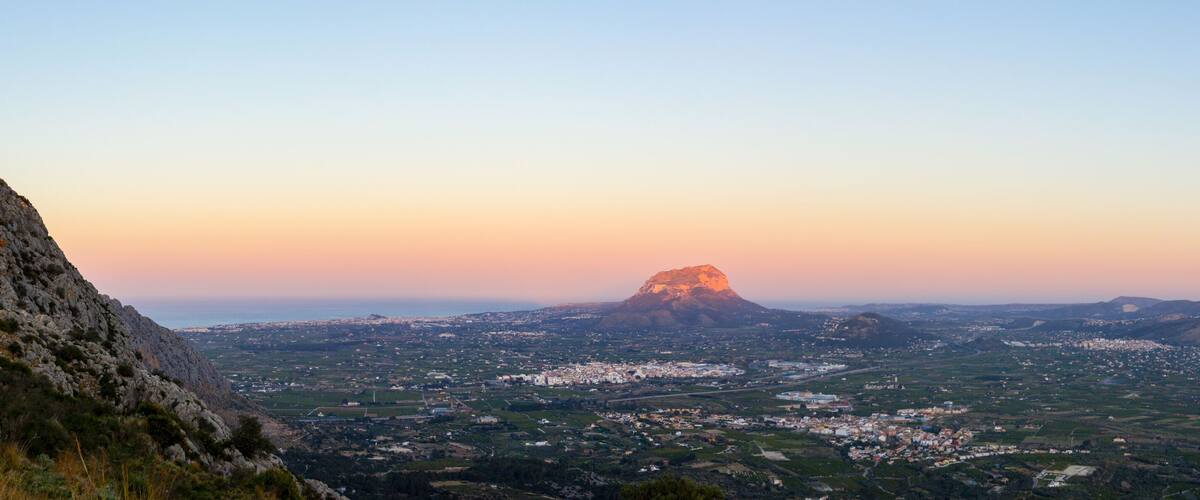 A mountainous landscape with a prominent peak in the distance and a valley with scattered buildings.