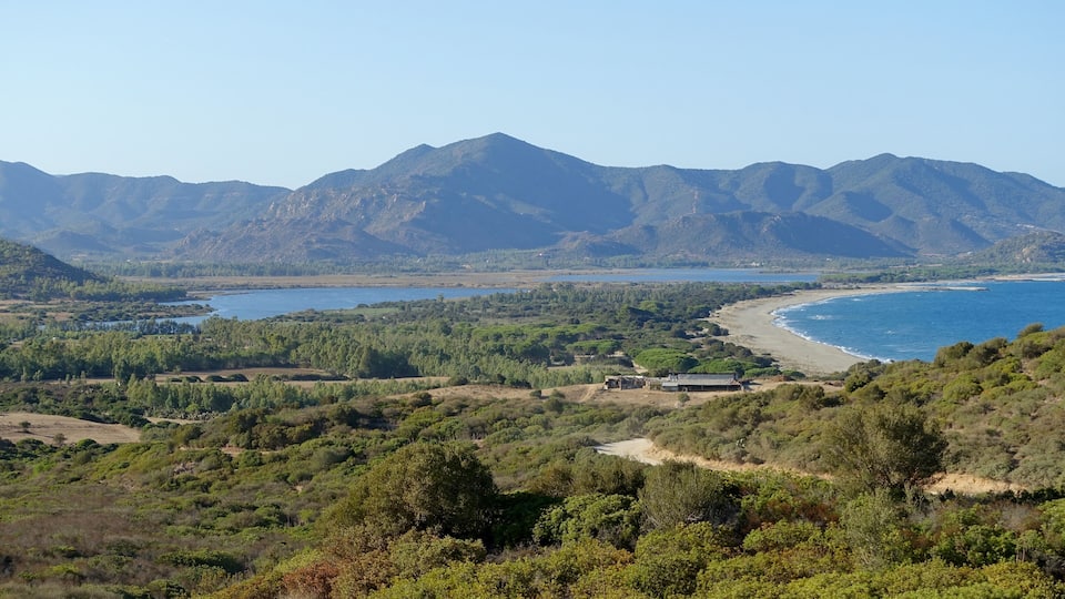 A coastal landscape with mountains, a beach, and dense vegetation.