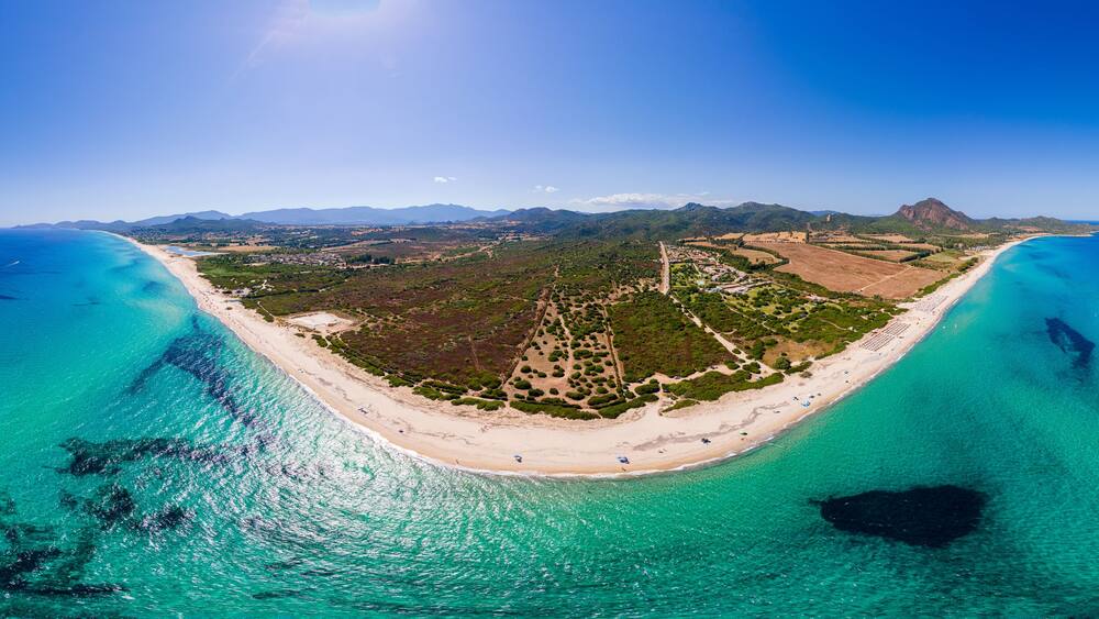 Eine Küstenlandschaft mit Strand, klarem türkisblauem Wasser und einem Bergpanorama im Hintergrund.