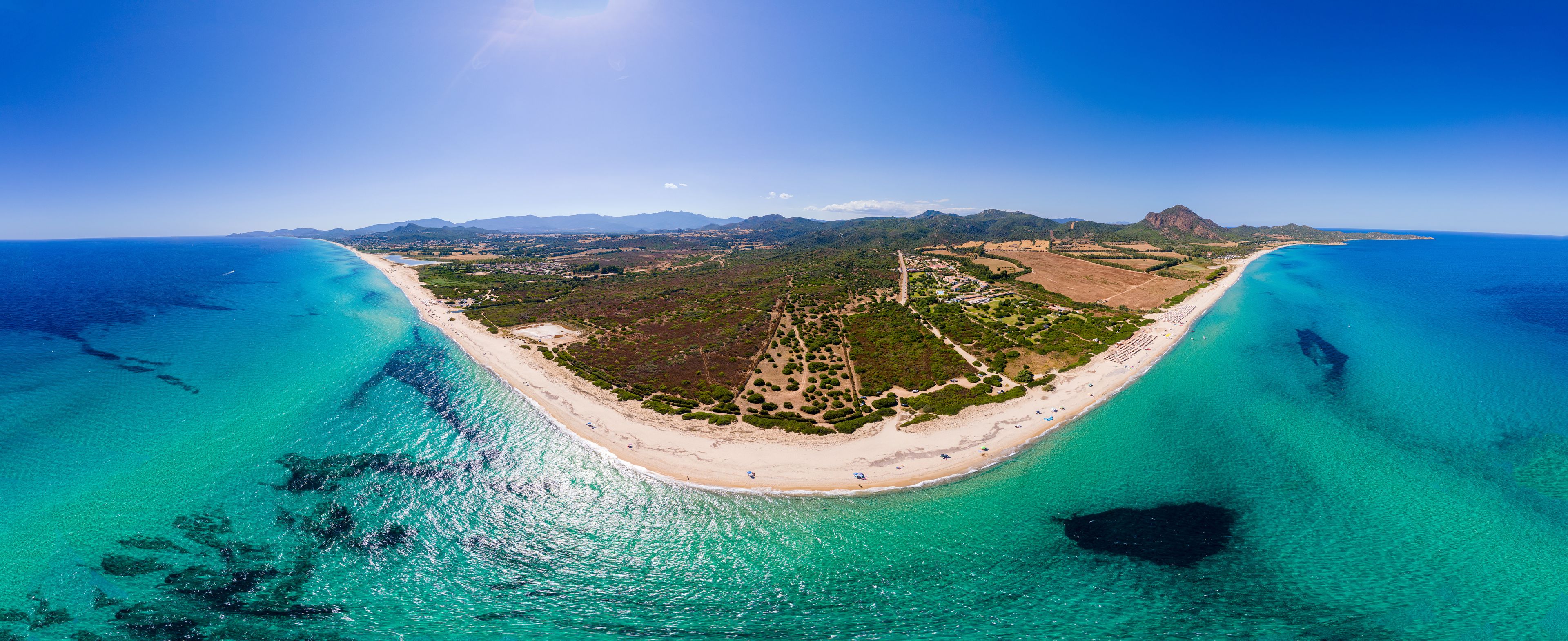A coastal landscape with a beach, clear turquoise waters, and a mountainous backdrop.