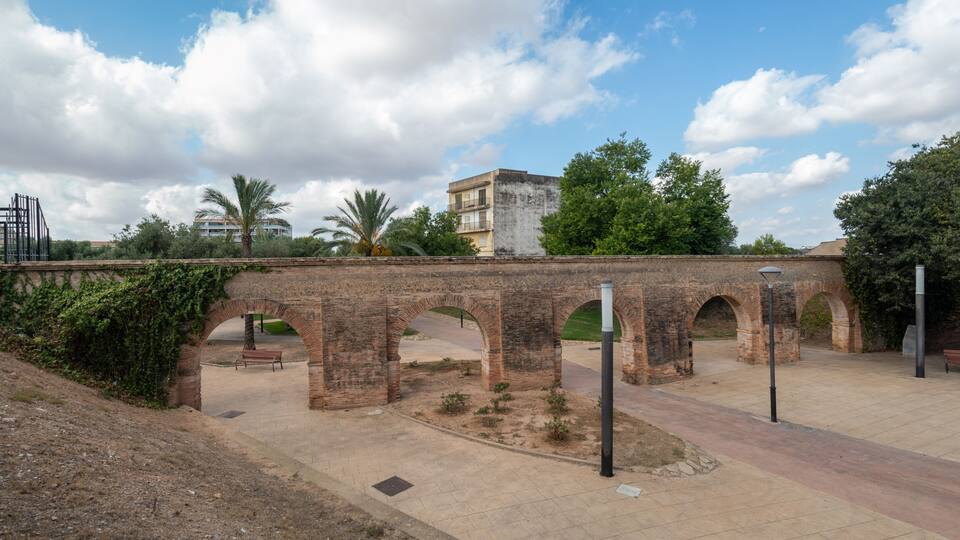 An ancient stone bridge with arches, a paved walkway, and a building in the background.