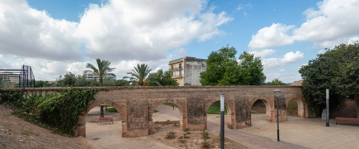 An ancient stone bridge with arches, a paved walkway, and a building in the background.