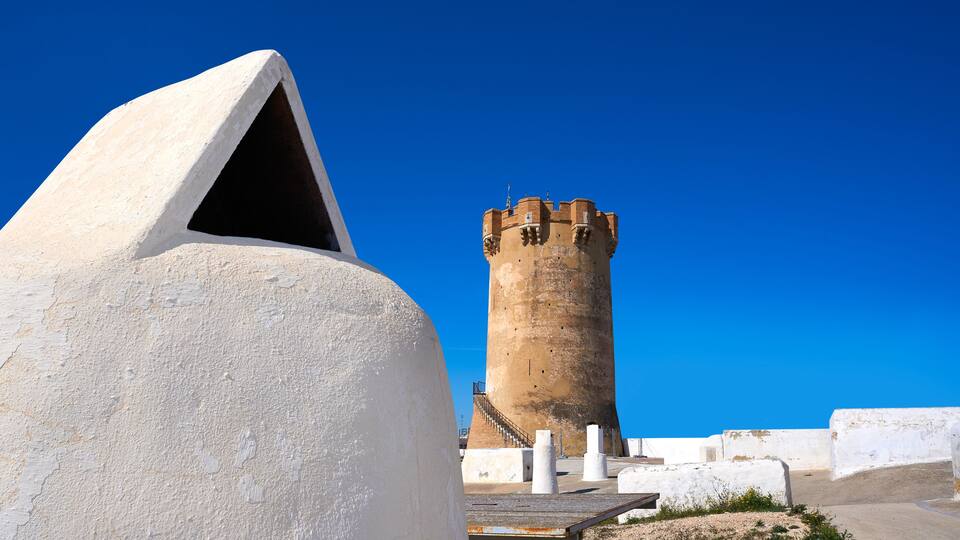 A white dome structure and a tall, cylindrical tower with crenellations under a clear blue sky.