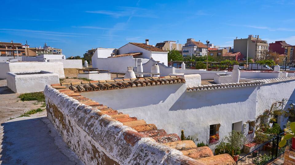 A rooftop with white walls and terracotta tiles, surrounded by buildings and greenery.