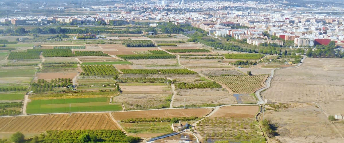 An aerial view of a city with extensive agricultural fields, a river, and a distant urban area.