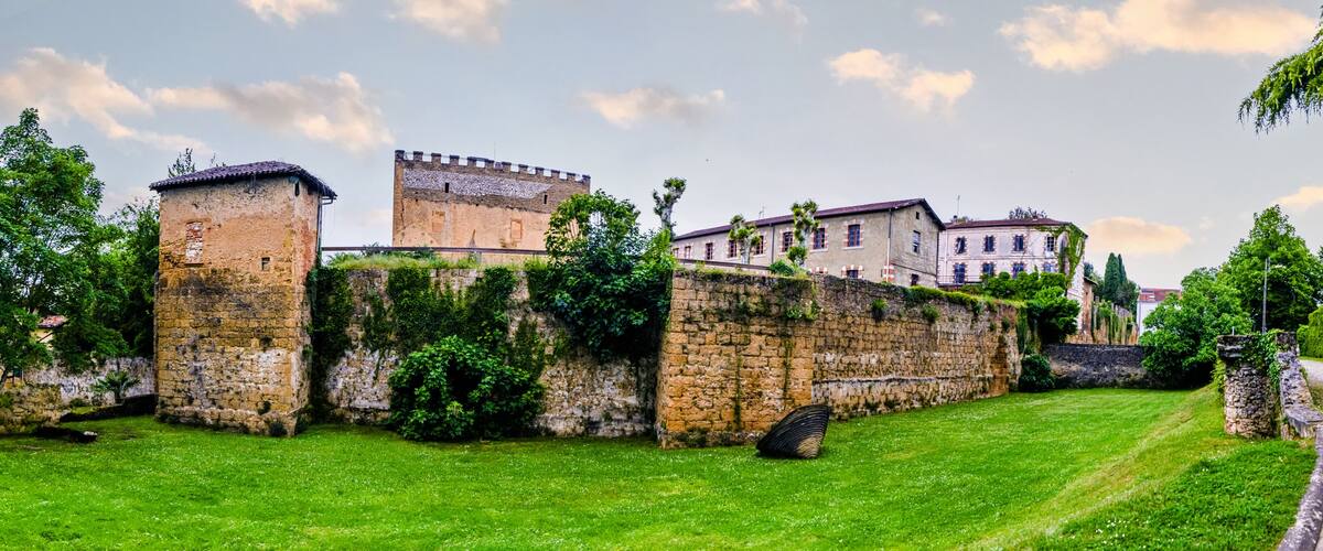 A historic stone wall with a castle in the background, lush green grass, and a clear sky.
