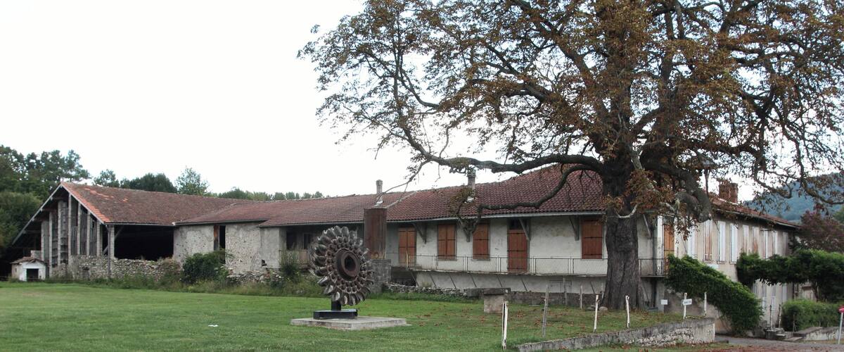 A rural building with a large windmill, a grassy field, and a paved road.