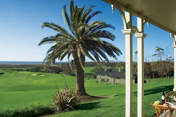 A golf course with a palm tree, a house, and a covered patio with a table and chairs.