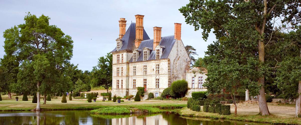A large, historic building with multiple chimneys and a pond reflecting its structure.