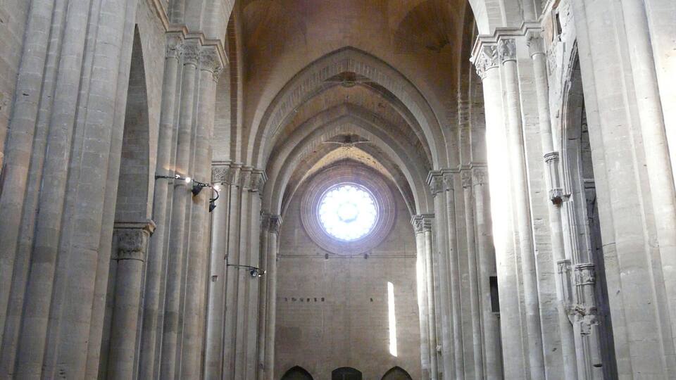 A cathedral interior with high vaulted ceilings, large columns, and a central circular window.