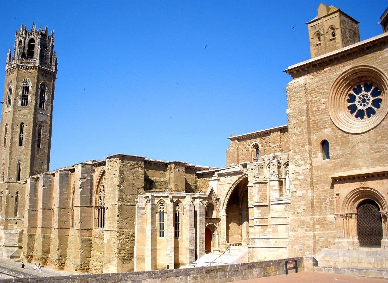 Un edificio histórico de piedra con una torre alta y un amplio ventanal circular.