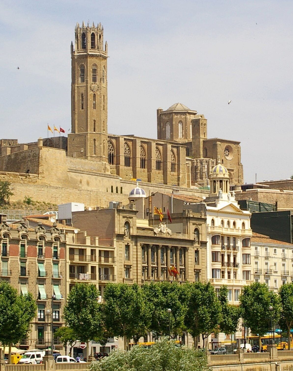 A historic building with a prominent tower and dome, surrounded by modern buildings and trees.