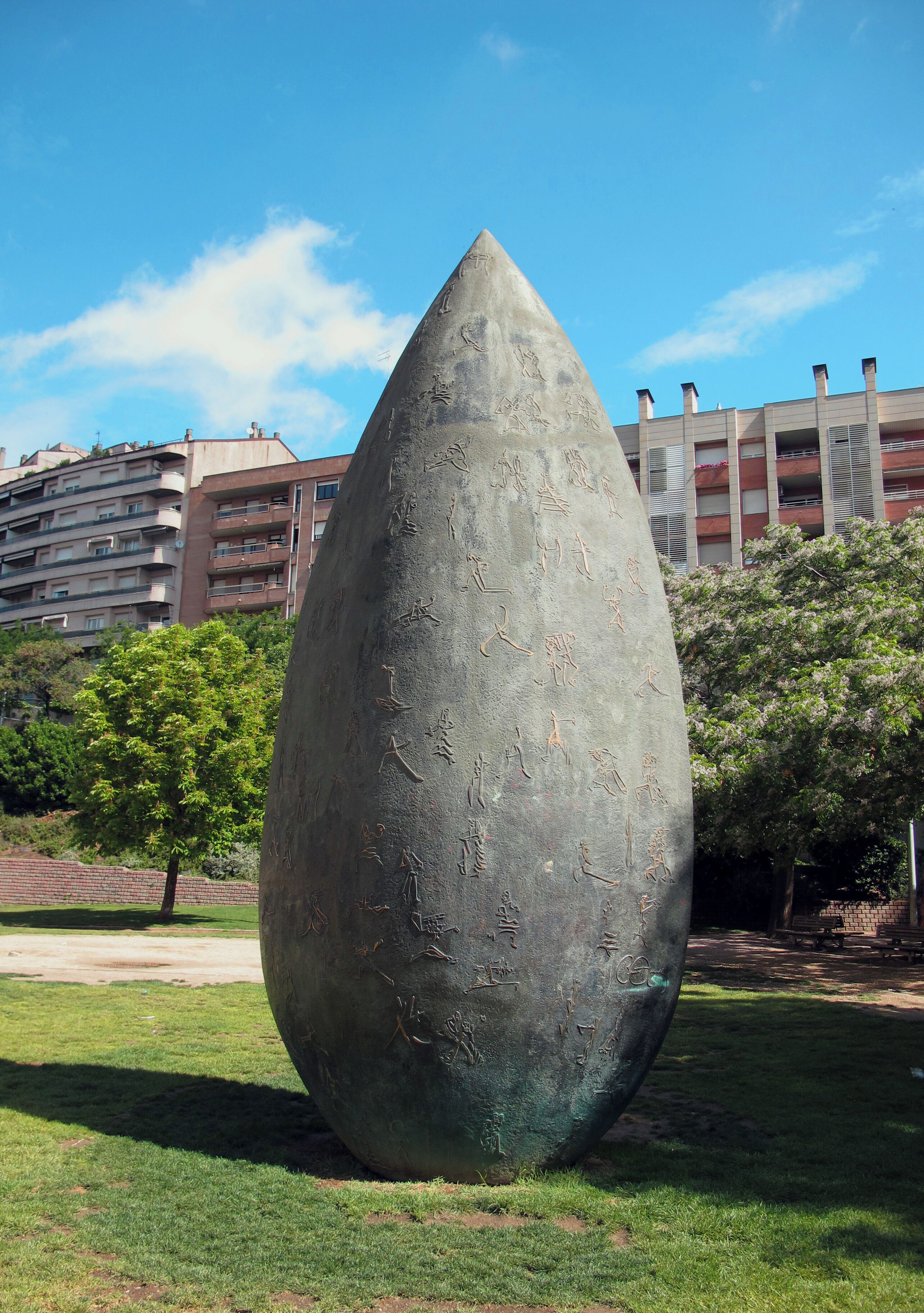 Una escultura grande y lisa de metal en un parque, con un edificio al fondo.