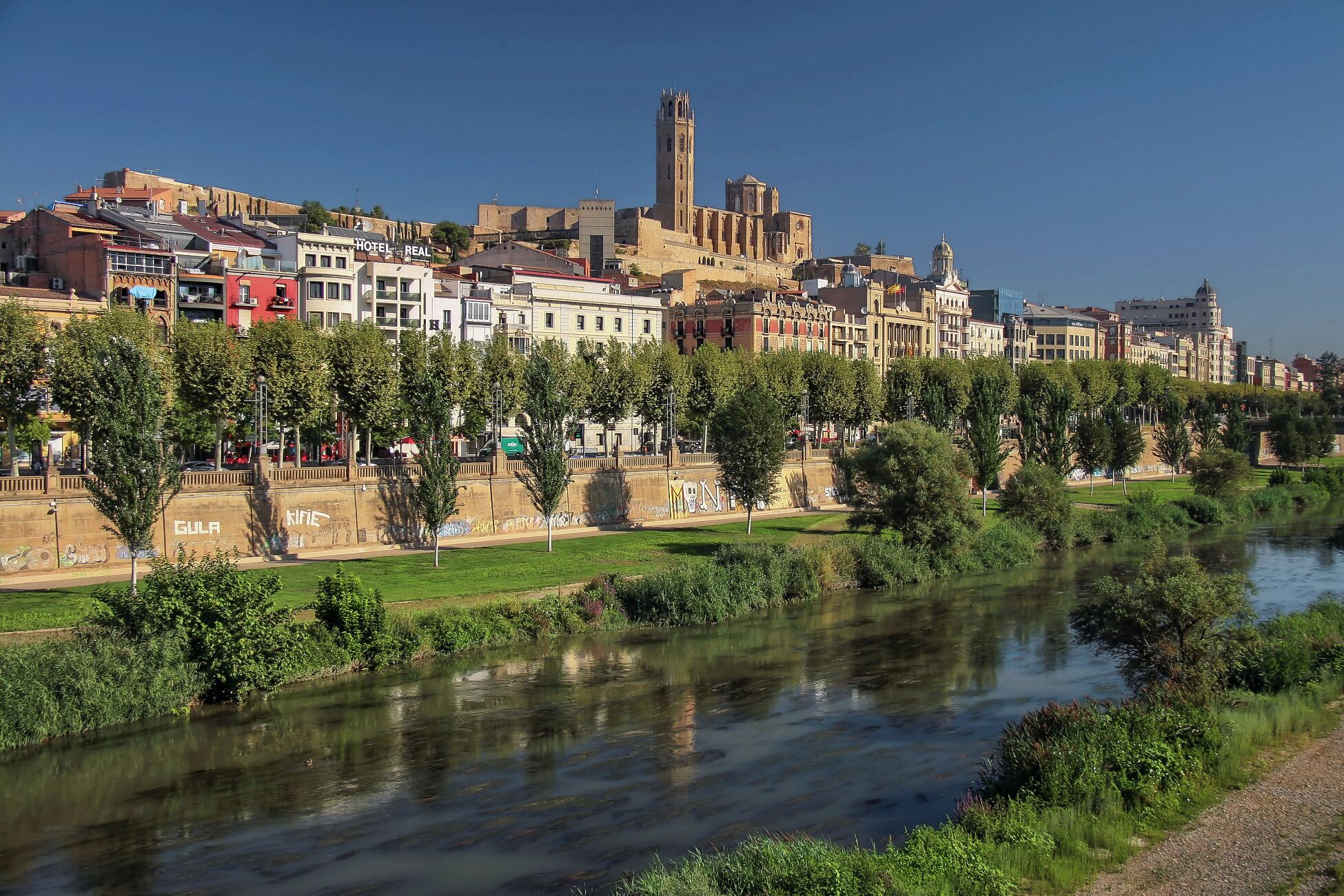 A river with a bridge, a historic building with a tower, and a row of colorful buildings along the riverbank.
