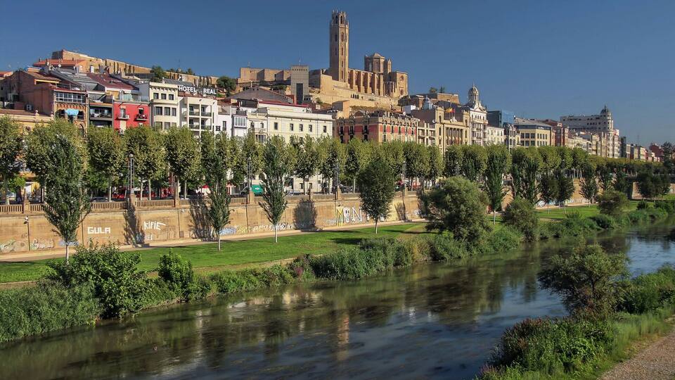 A river with a bridge, a historic building with a tower, and a row of colorful buildings along the riverbank.