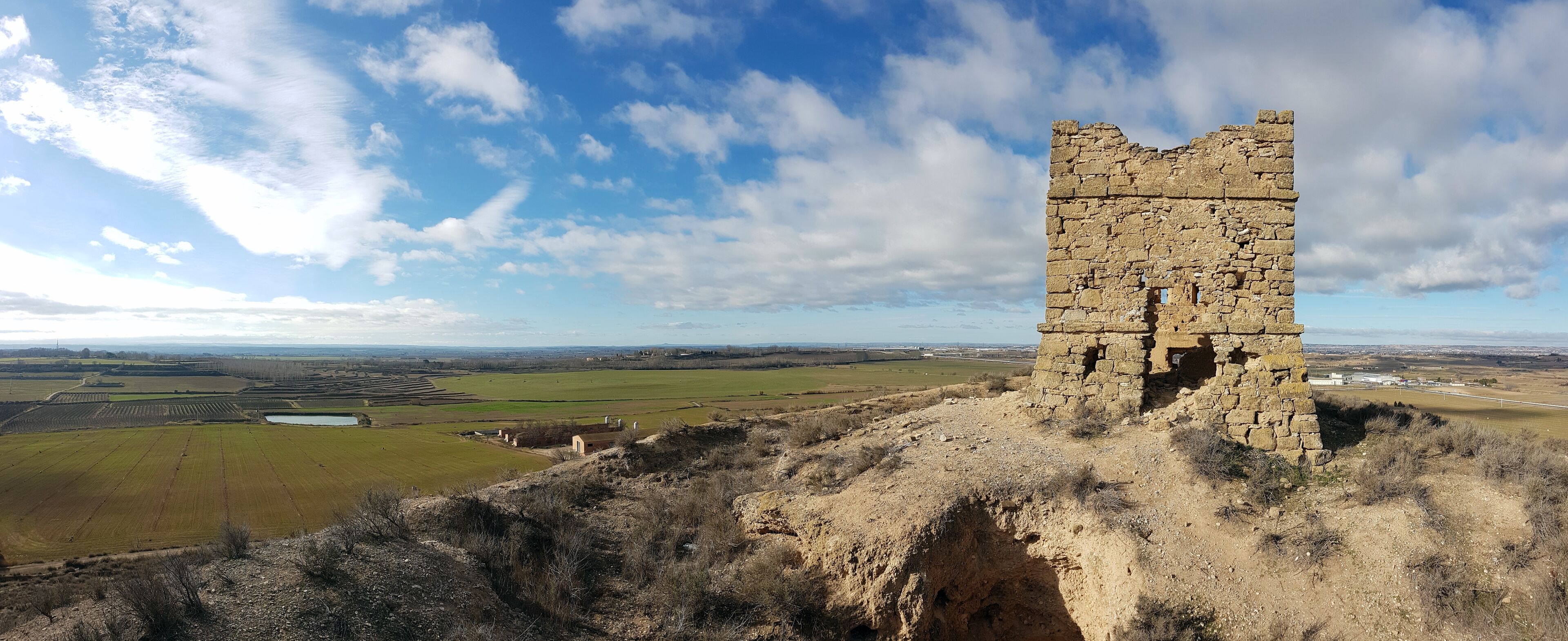 A stone tower on a hill with a view of fields and distant buildings.