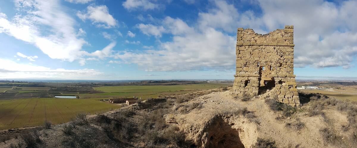 A stone tower on a hill with a view of fields and distant buildings.