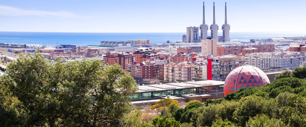 A coastal cityscape with modern architecture, including a distinctive red building and a large spherical structure.