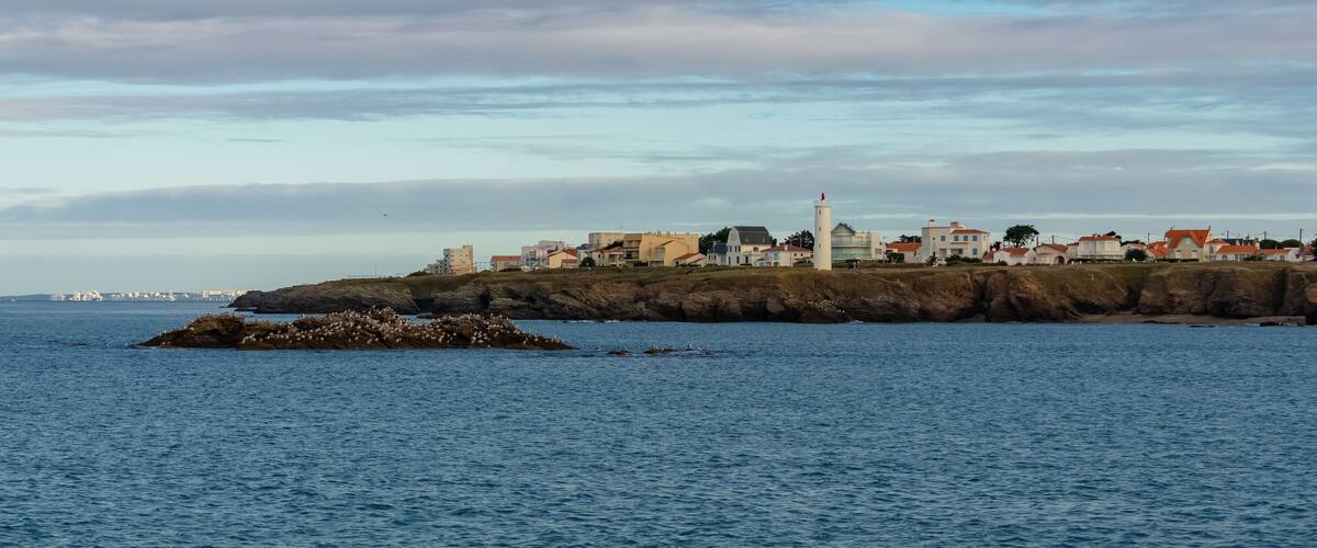 A coastal town with buildings, a lighthouse, and rocky outcrops.