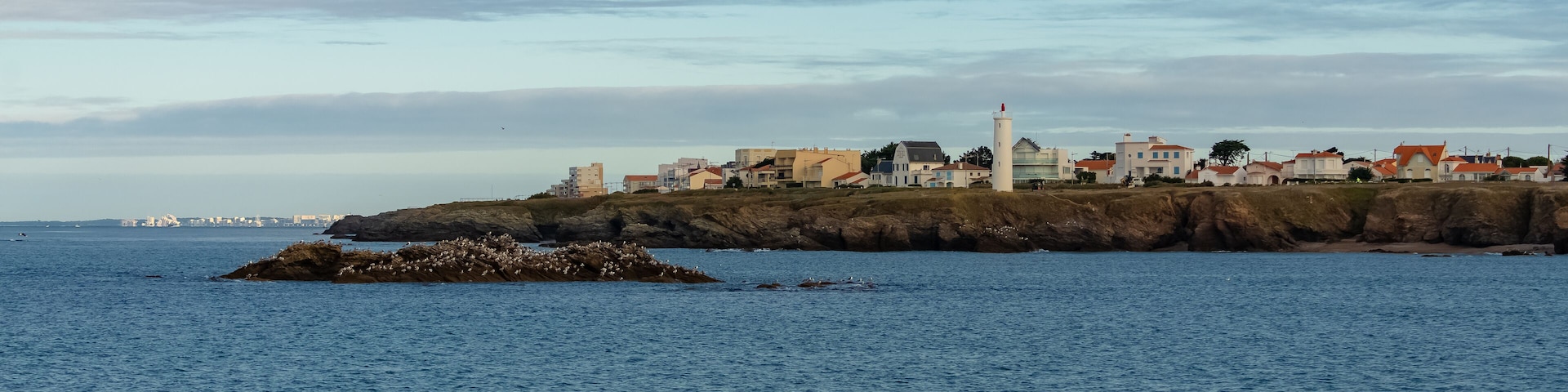 A coastal town with buildings, a lighthouse, and rocky outcrops.