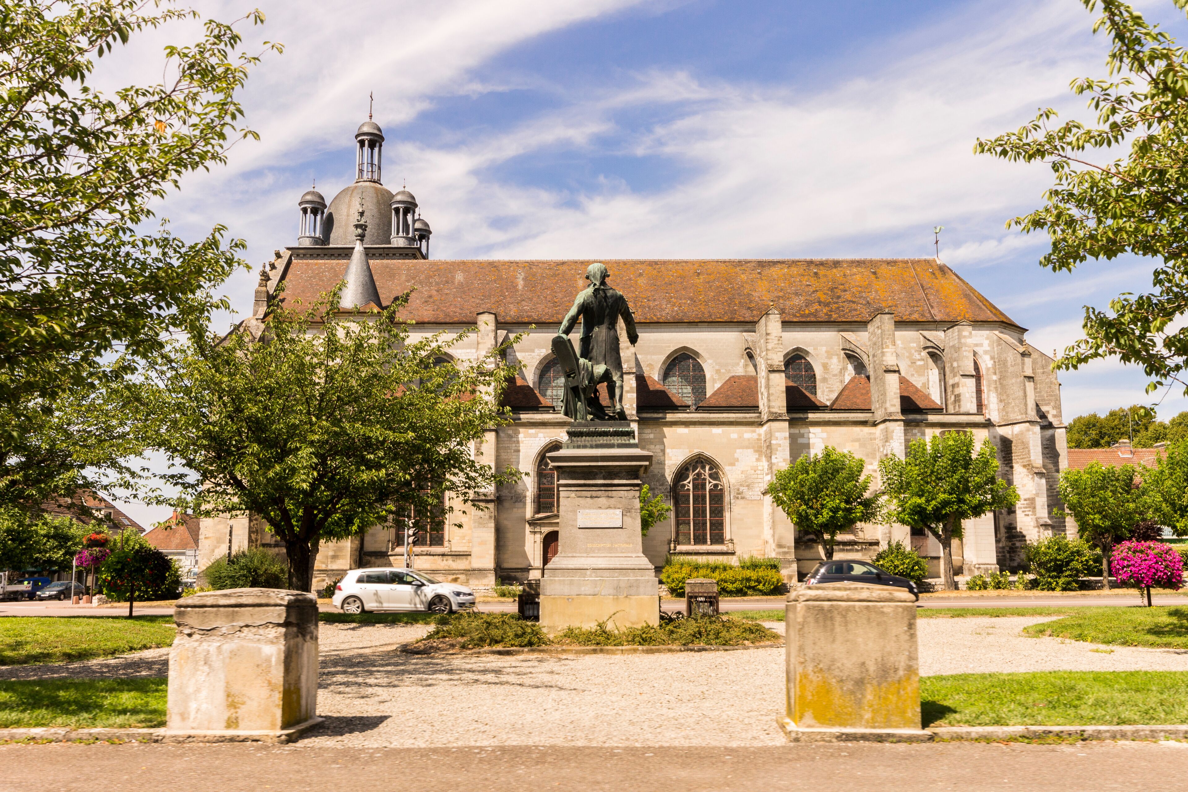 A historic church with a statue in front, surrounded by trees and a clear sky.