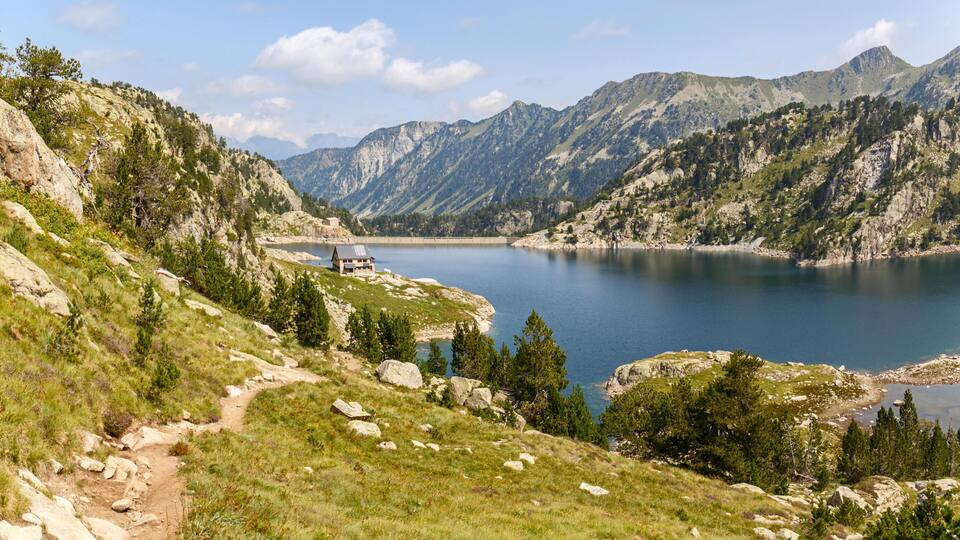 A mountainous landscape with a lake, a small building, and a path.